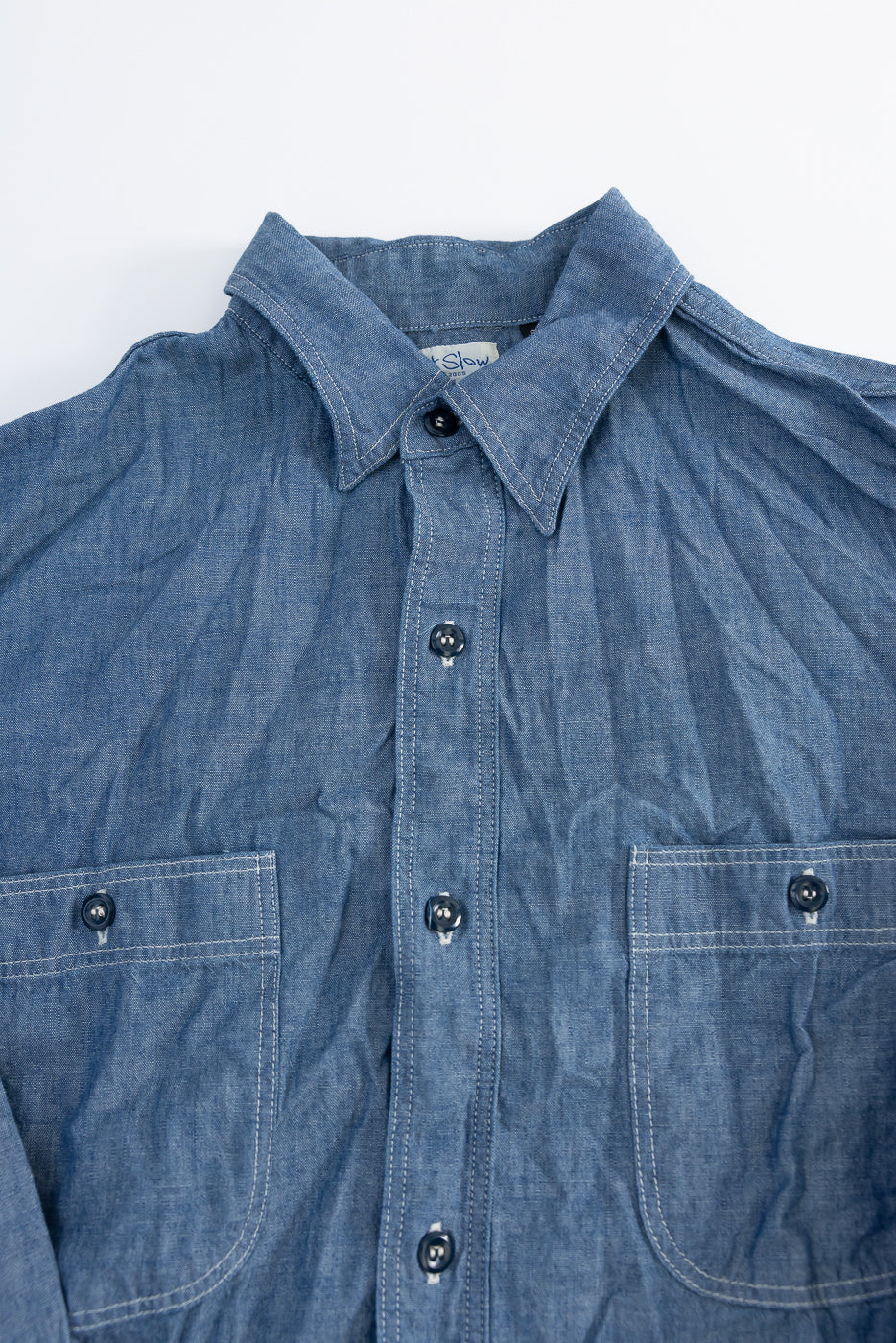 Close-up front view of indigo chambray work shirt, showing collar, buttons, and chest pockets.