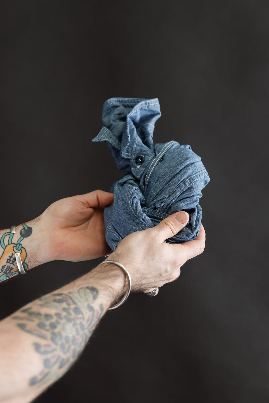 Close-up of hands holding indigo chambray work shirt, showing fabric texture and buttons.