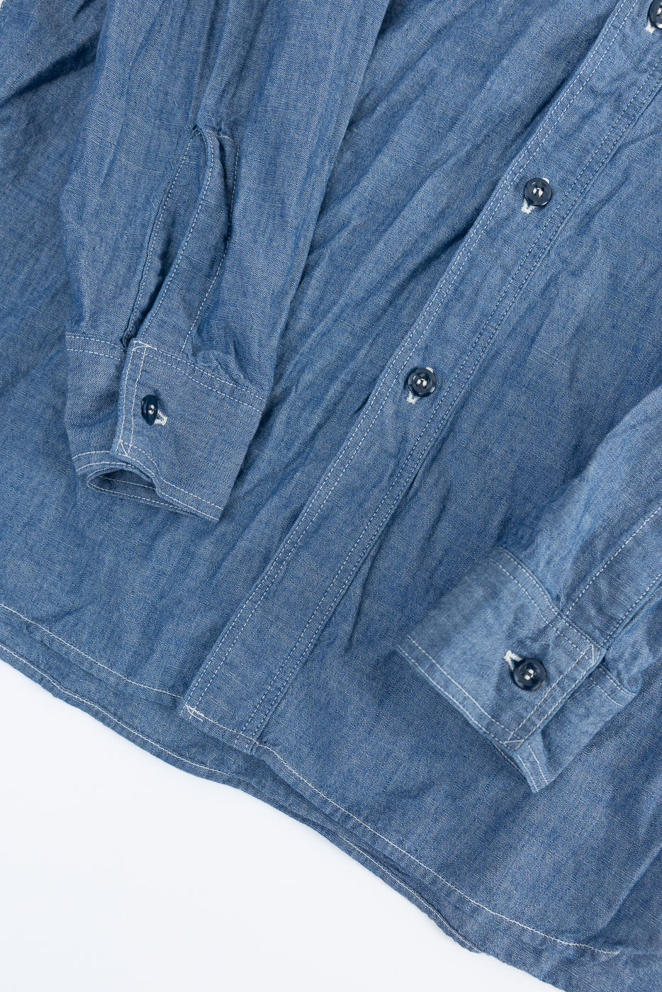Close-up of front lower section of indigo chambray work shirt showing buttons, cuffs, and fabric texture.