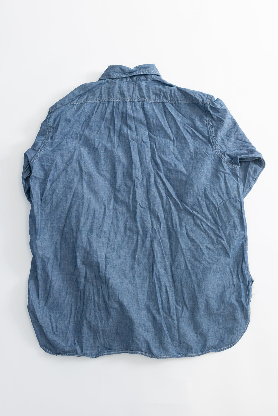 Flat lay of indigo chambray work shirt, back view showing yoke and curved hem detail.