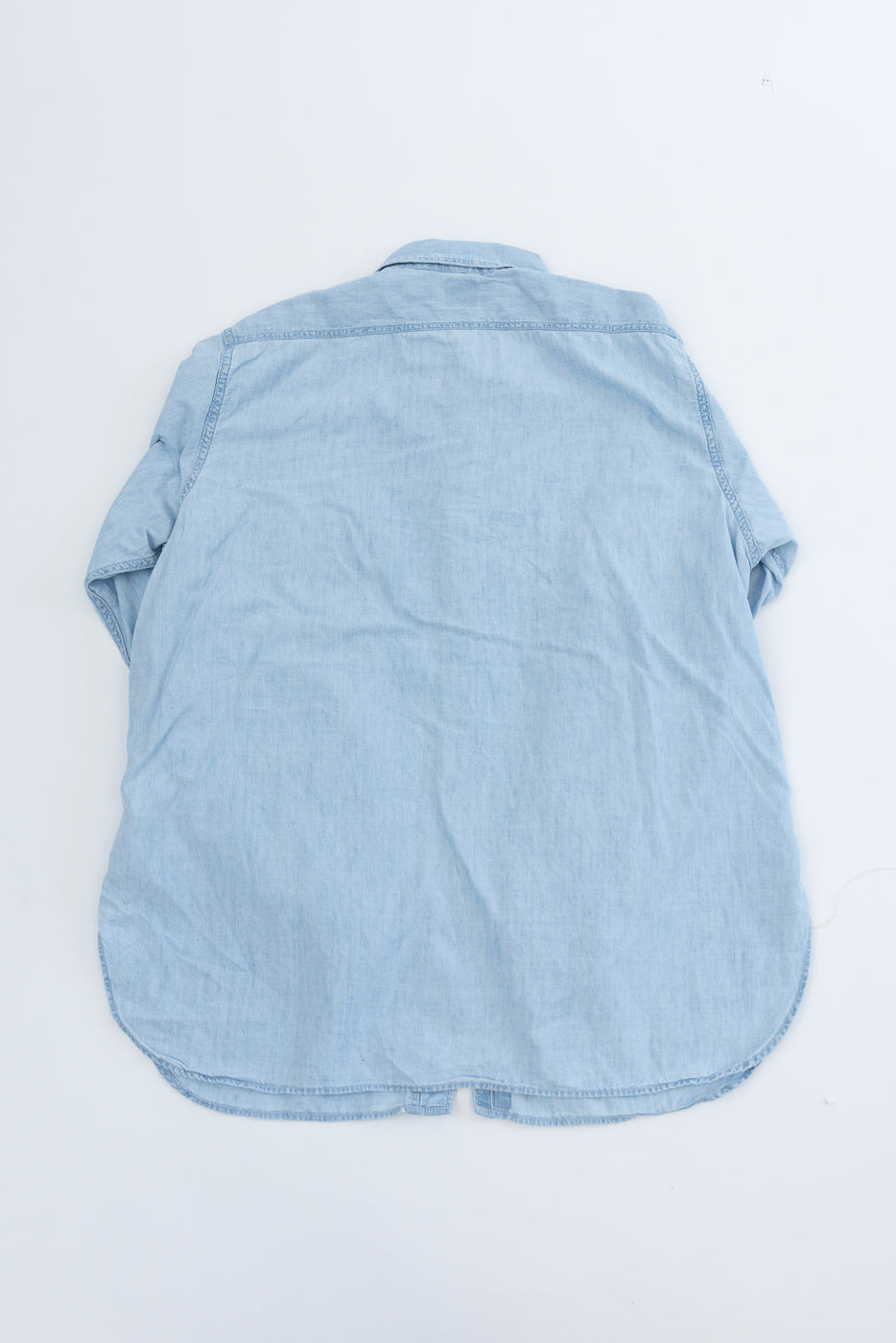 Back view flat lay of bleached chambray work shirt showing yoke, curved hem, and texture