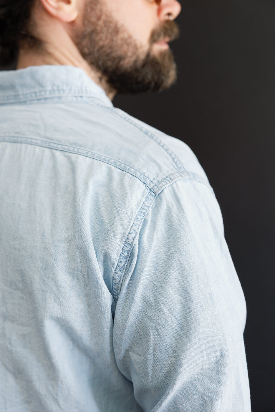 Close-up of the back shoulder and collar of a light chambray work shirt on a male model, 5'9