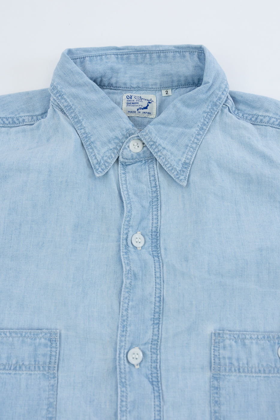 Close-up front view of light blue chambray work shirt with button details and pointed collar.