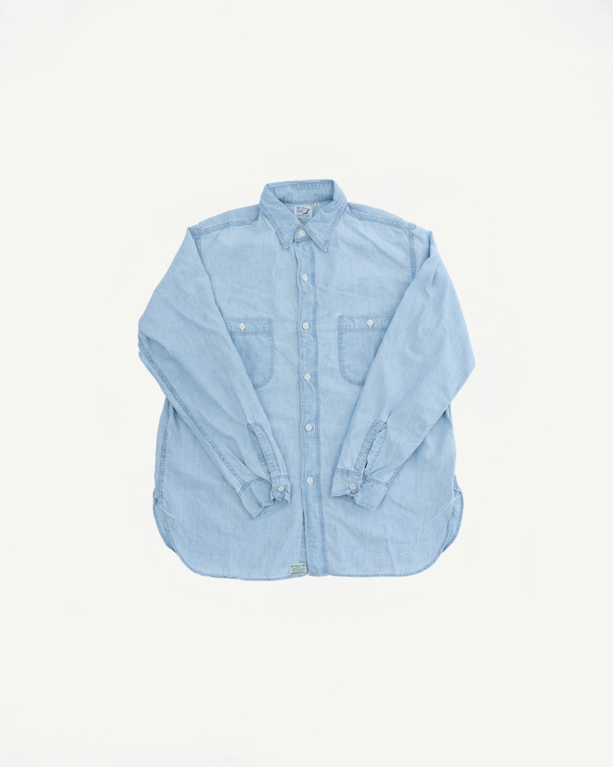 Flat lay, front view of light blue chambray work shirt with button front and chest pockets.