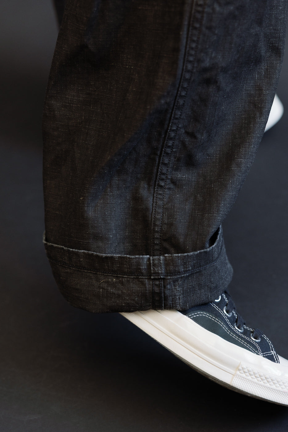 Close-up of dark selvedge jeans hem, cuffed, worn by male model, paired with navy sneakers