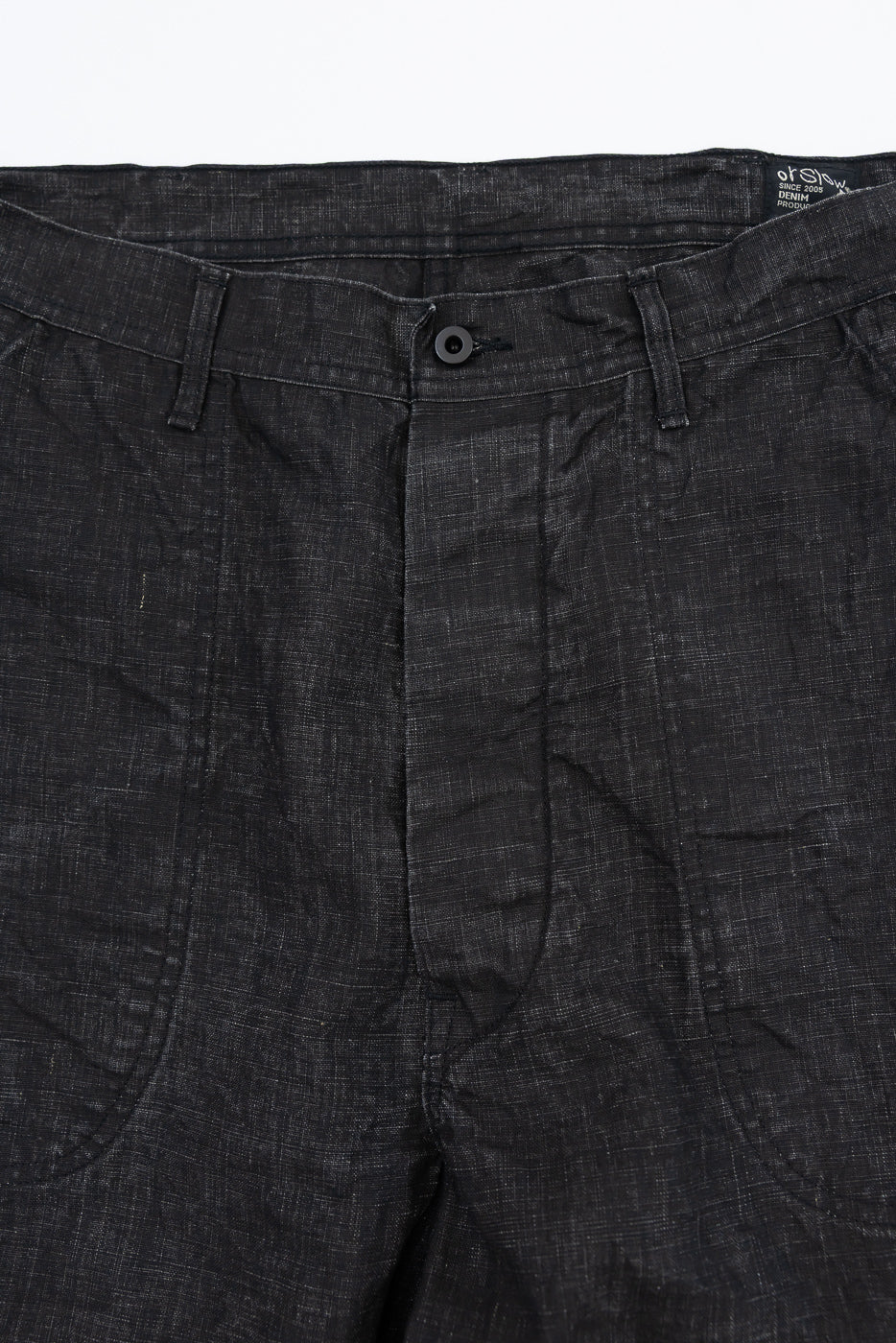Close-up front view of dark selvedge denim pants with button fly and textured fabric detail