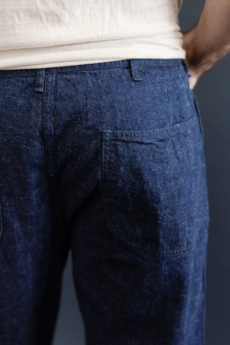 Close-up of back side of indigo denim utility pants on male model, showing rear pocket and texture, model is 5'9