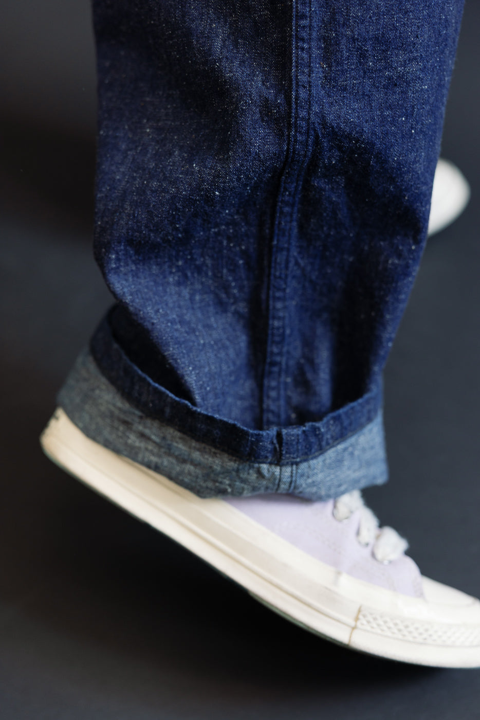 Close-up of male model’s lower leg wearing indigo selvedge denim utility pants, side view, showing hem details. Model is 5'9