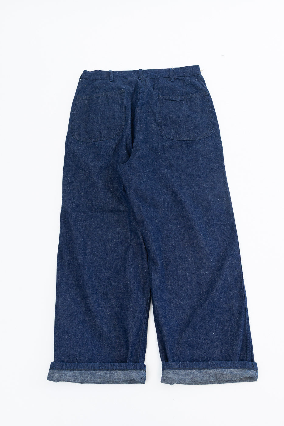 Flat lay showing back view of indigo selvedge denim wide fit utility pants with cuffed hem and back patch pockets.