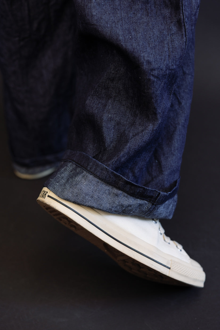 Close-up of male model's rolled denim hem with white sneakers, showcasing fabric texture and fit.