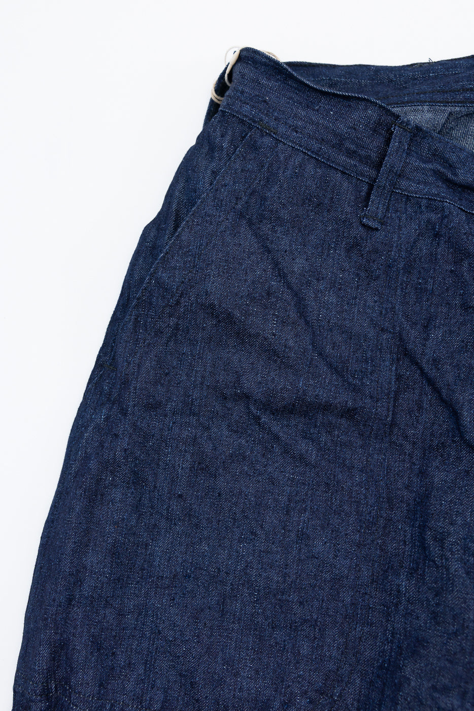 Close-up front view of dark selvedge denim pants, showing waistband, button, and fabric texture