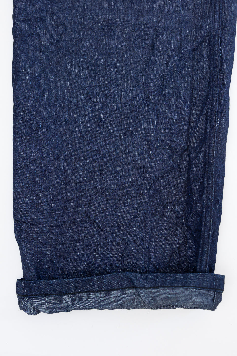 Close-up of dark blue selvedge denim pants, front view, showcasing fabric texture and rolled hem detail.