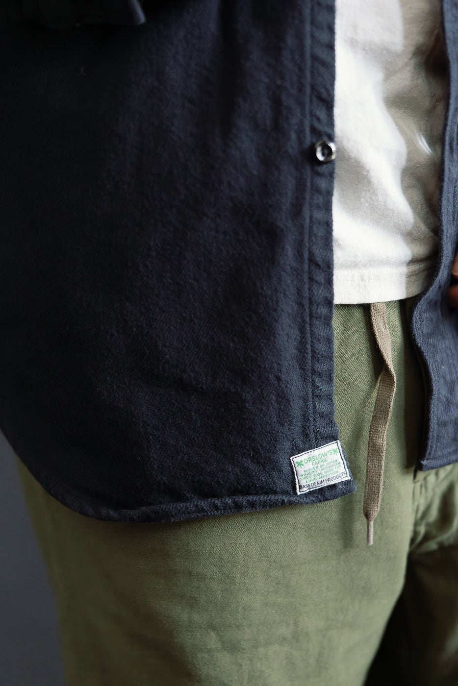 Close-up front hem of Orslow navy flannel shirt on male model, showing fabric texture and tag.