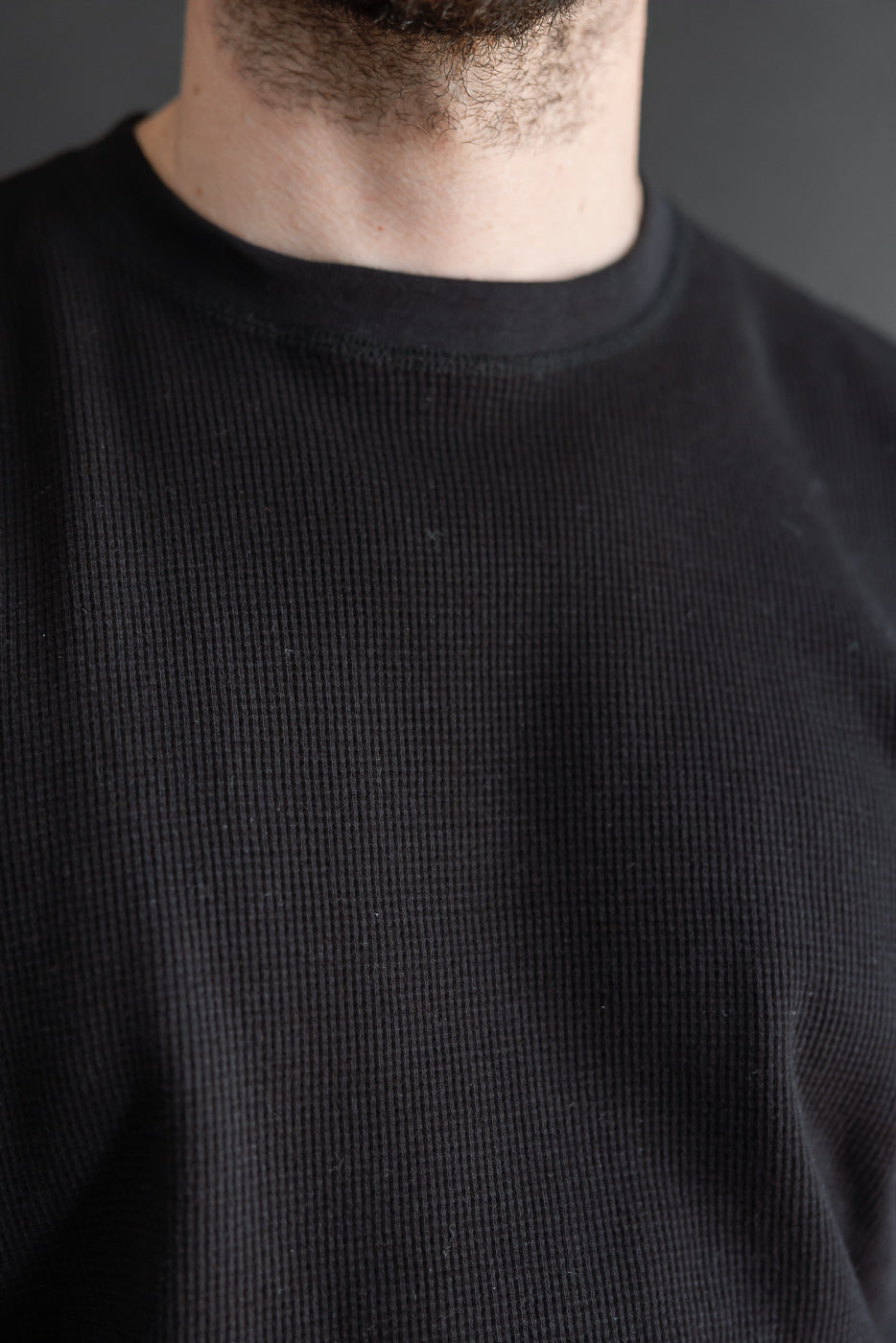 Close-up of the front neckline and waffle knit fabric texture on a black long-sleeve shirt.