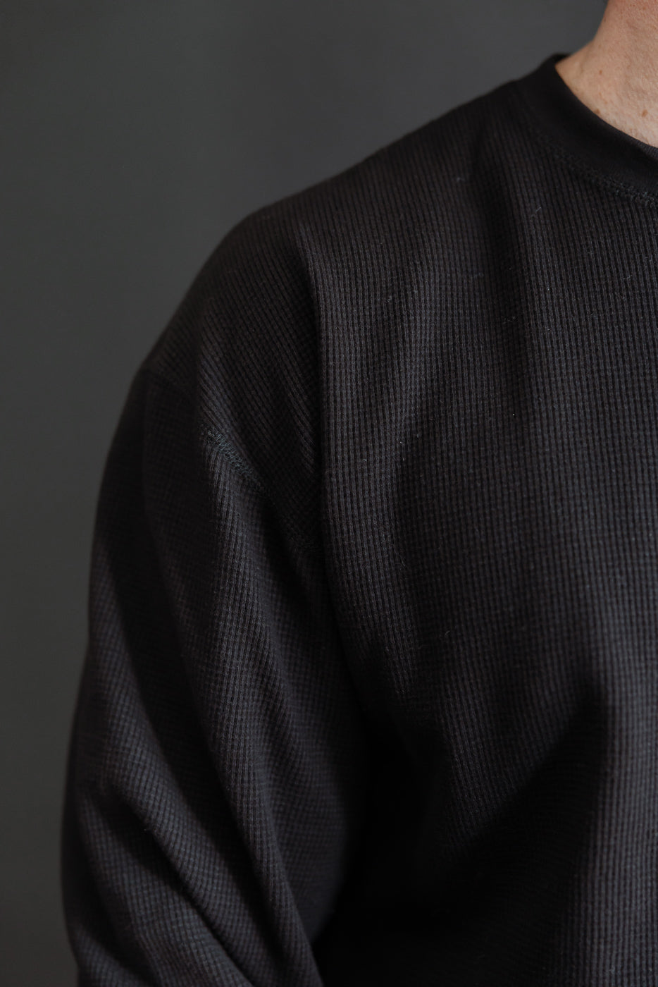 Close-up of the left side and sleeve texture of a black ribbed crewneck sweatshirt.