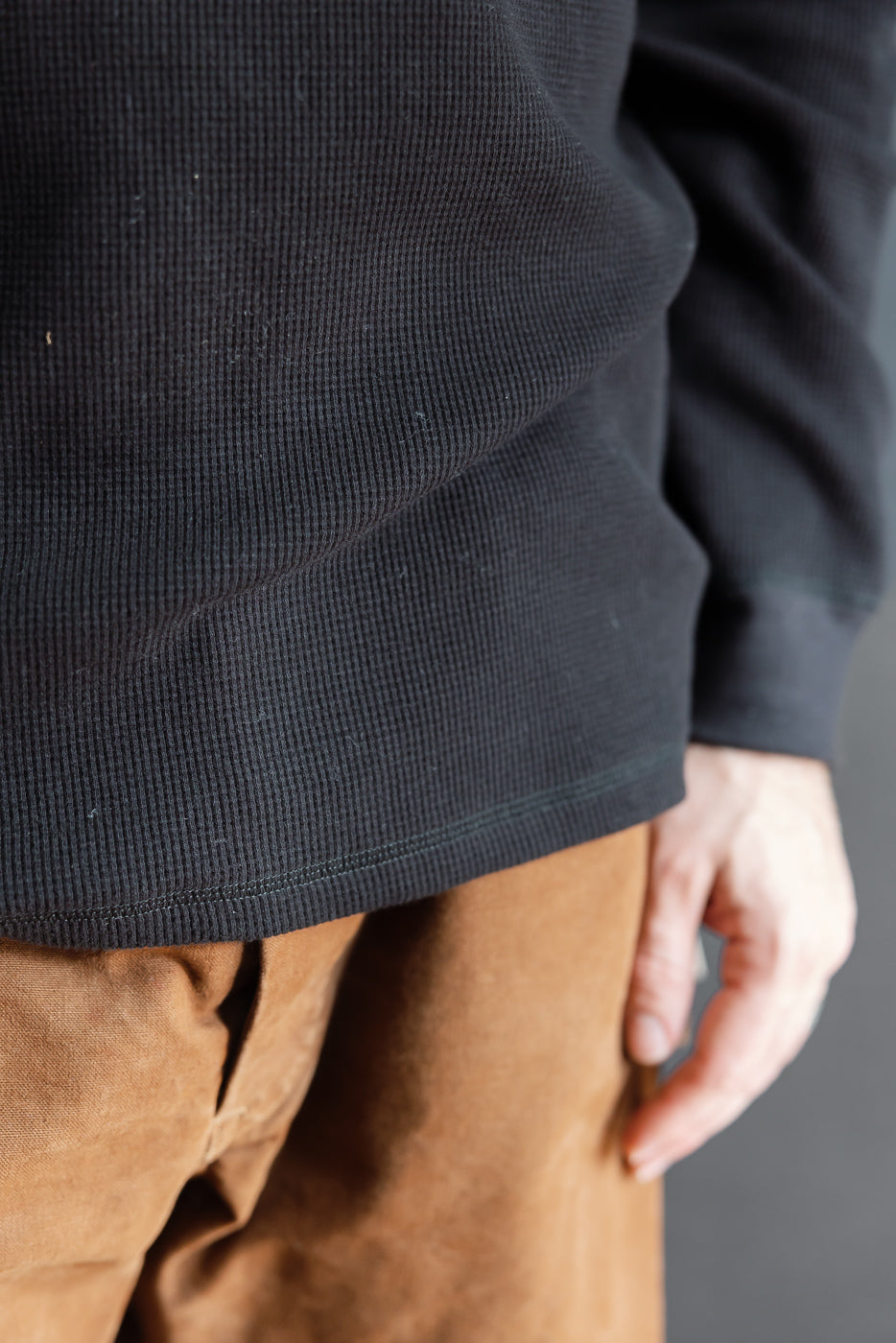 Close-up front view of a male model wearing a black waffle knit long-sleeve shirt and tan trousers.