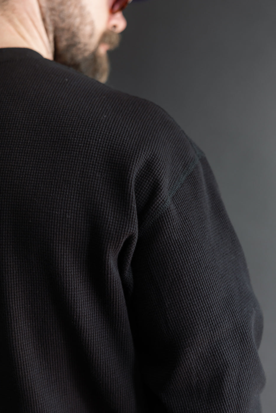 Close-up of the back and right sleeve of a black waffle knit thermal shirt on a male model.