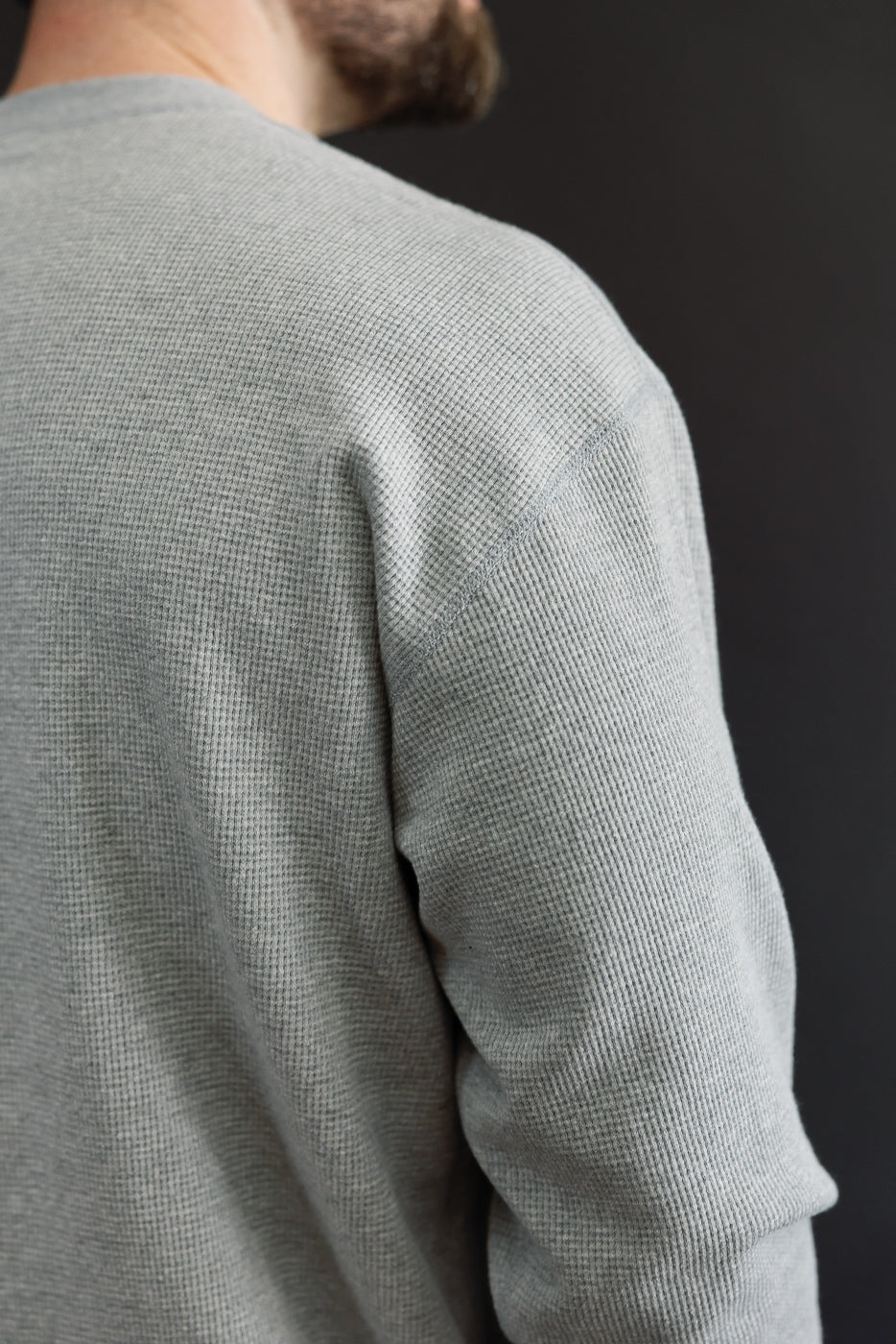 Close-up back view of a male model wearing a grey waffle knit long sleeve shirt.