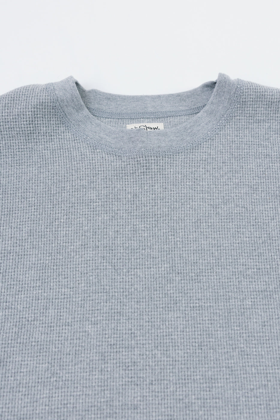 Close-up of the front neckline and waffle texture of a grey shirt showing the brand tag.