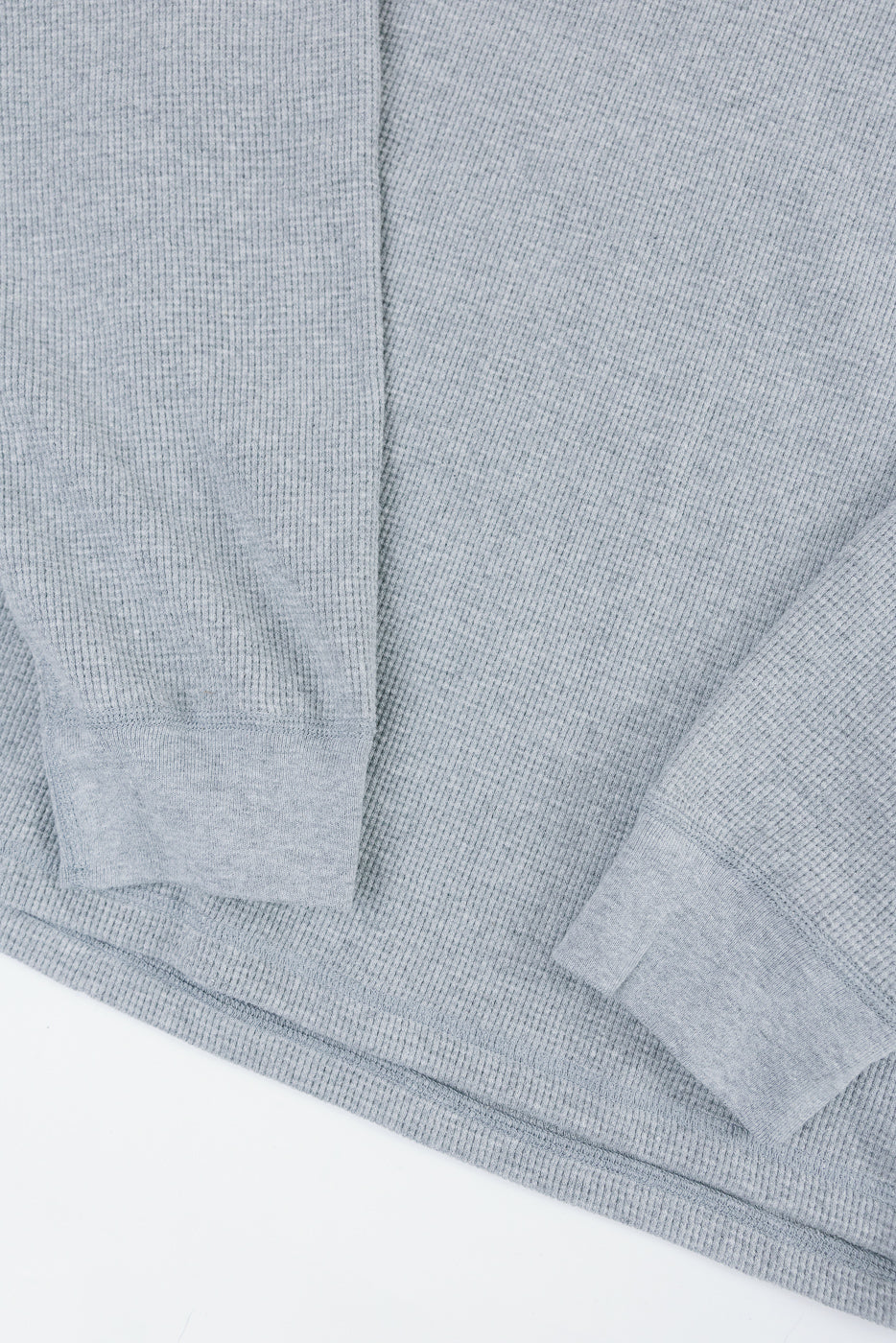 Close-up of the front texture and ribbed cuffs of a grey waffle knit long sleeve shirt.