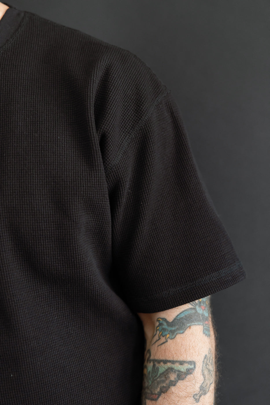 Close-up side view of a black waffle knit t-shirt sleeve texture on a male model.