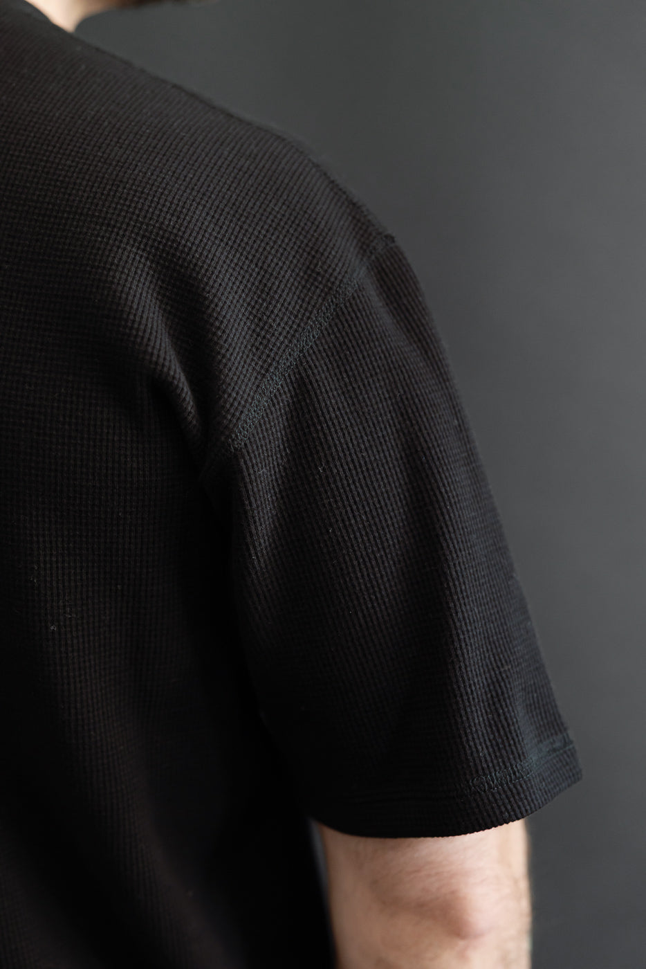 Close-up of the right sleeve and shoulder of a black waffle knit t-shirt.