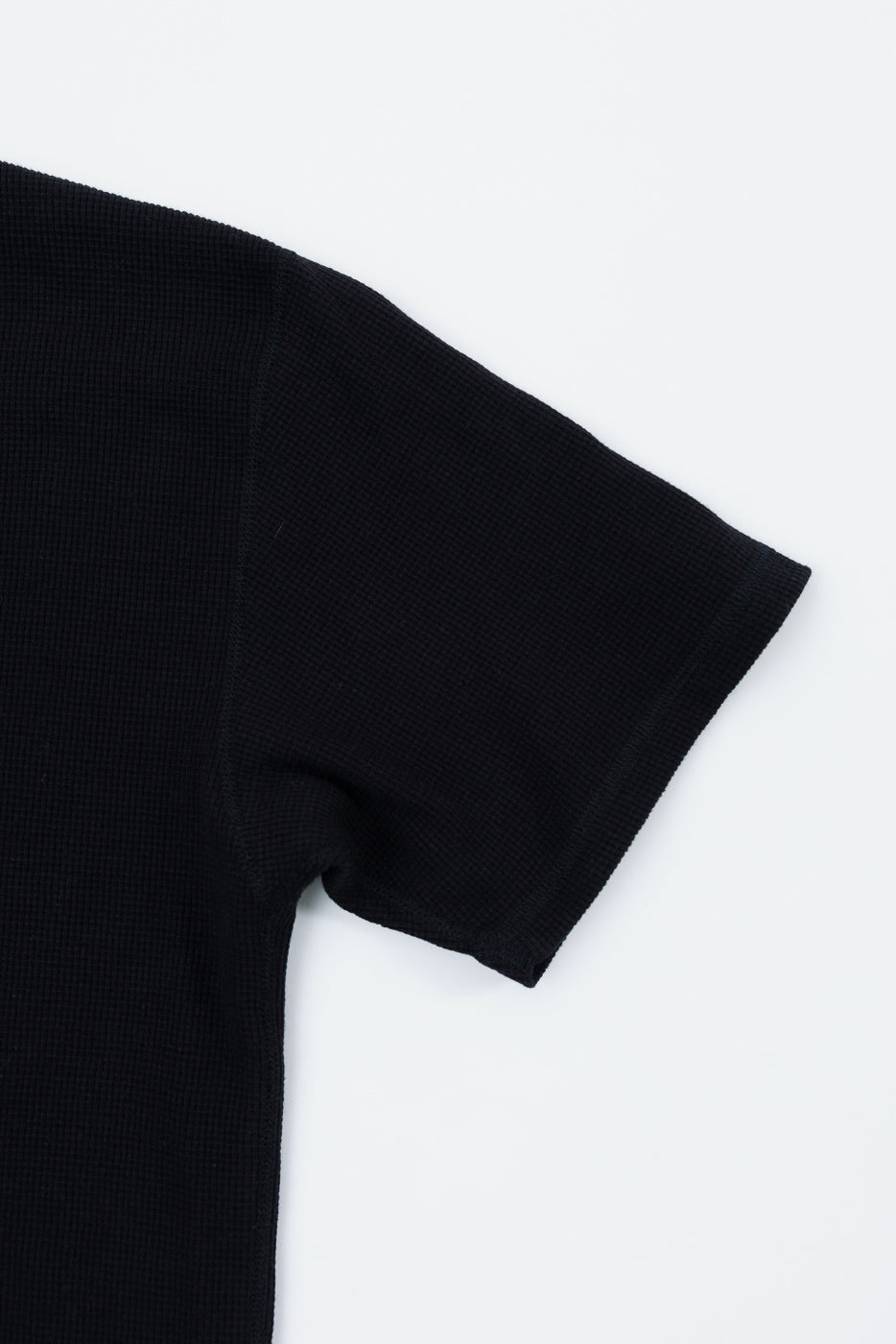Close-up of the left sleeve and shoulder of a black waffle-knit fabric garment.