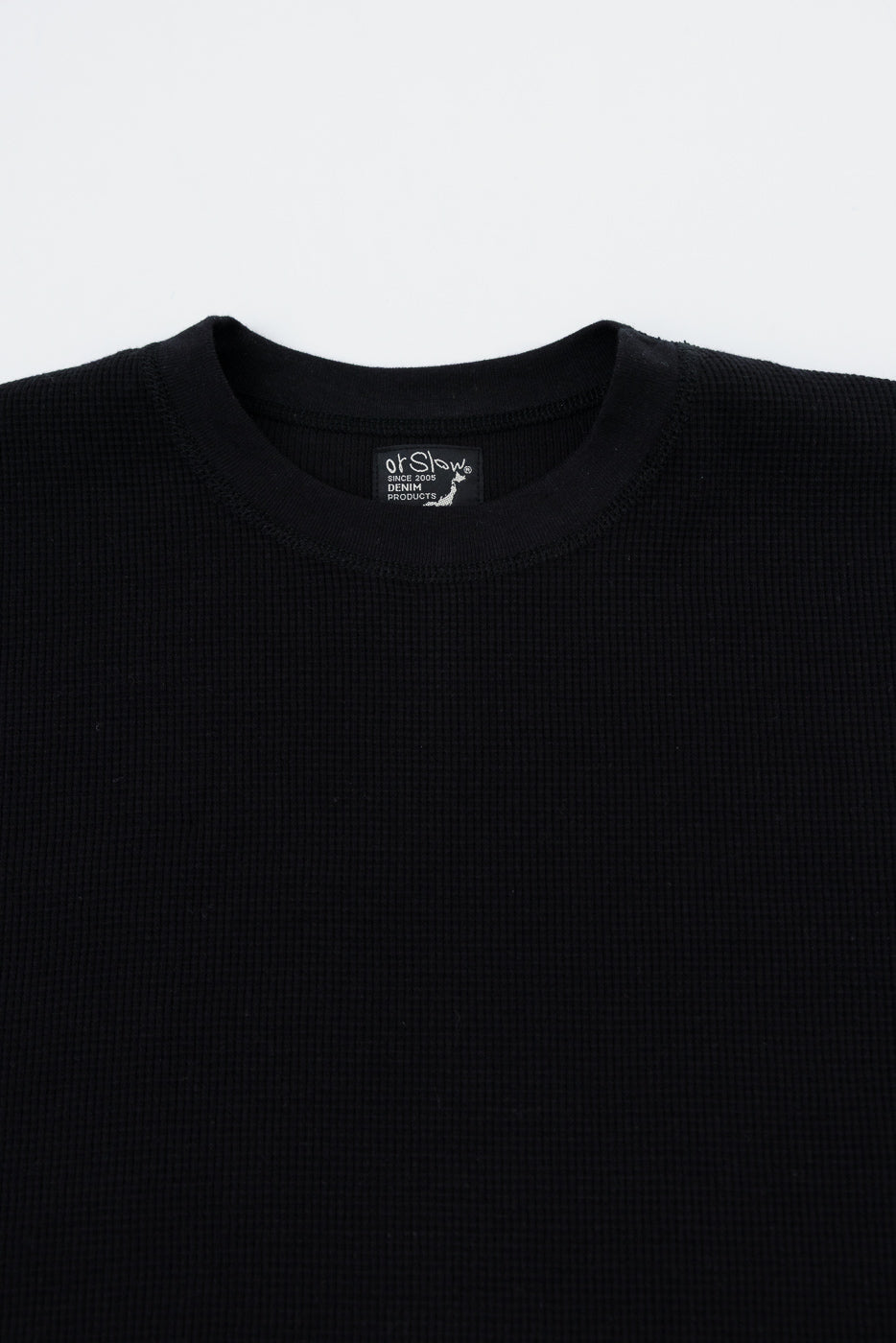 Close-up of the front neckline and inner tag of a black waffle knit crewneck sweater.