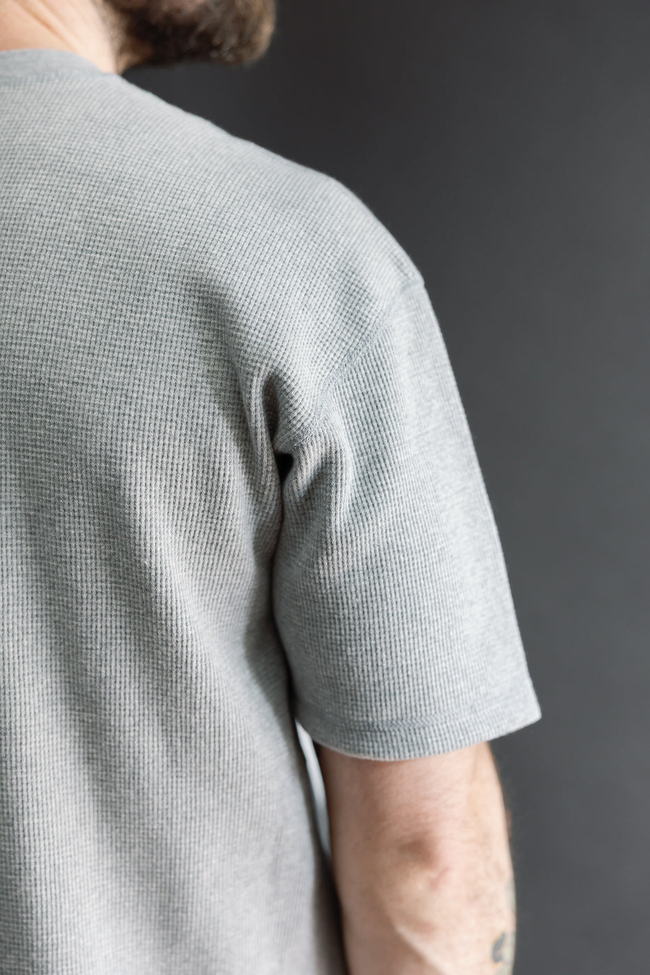 Close-up side view of a gray waffle knit t-shirt sleeve and shoulder on a male model.