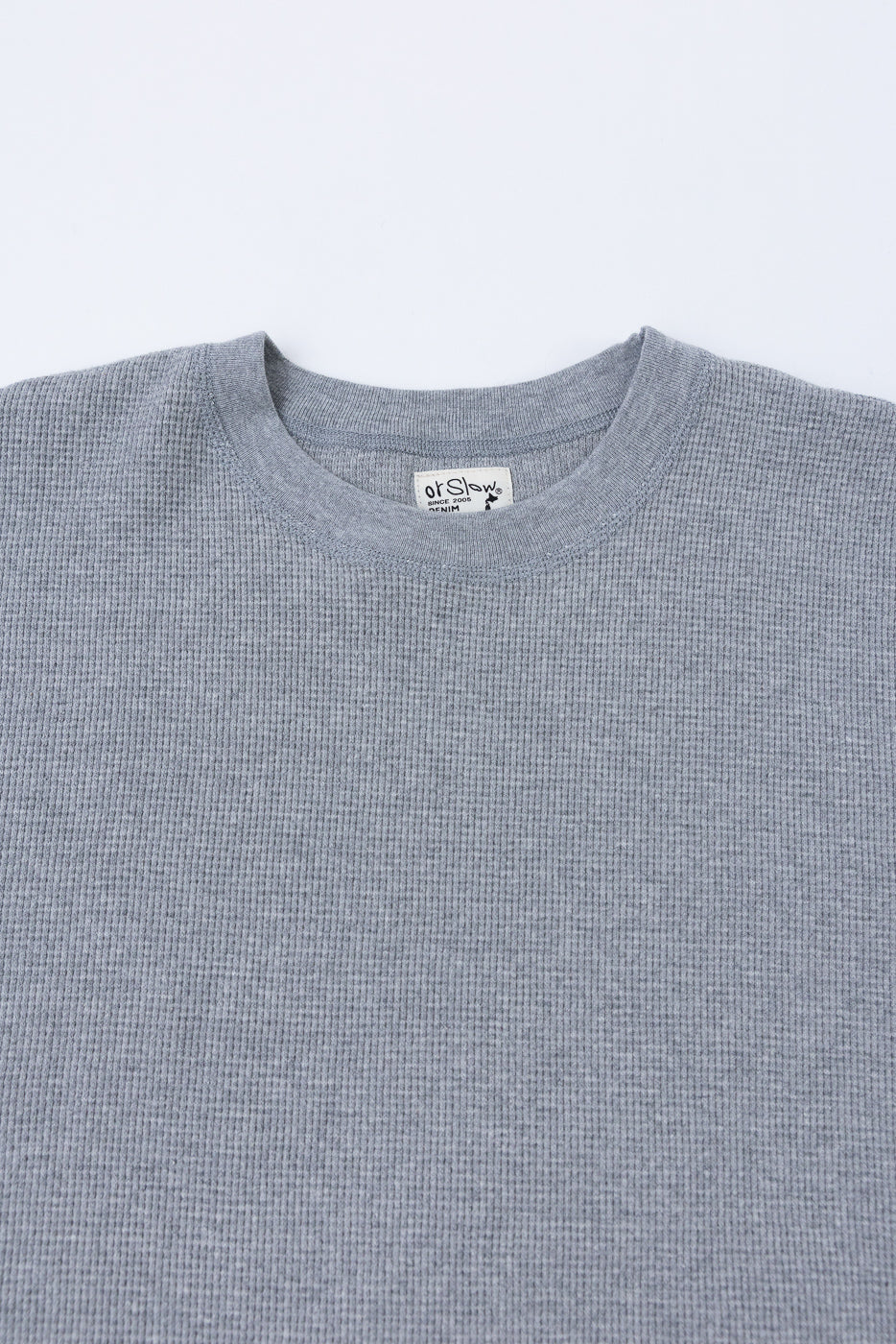 Close-up front view of a grey waffle knit crewneck sweater showing the ribbed collar and tag.