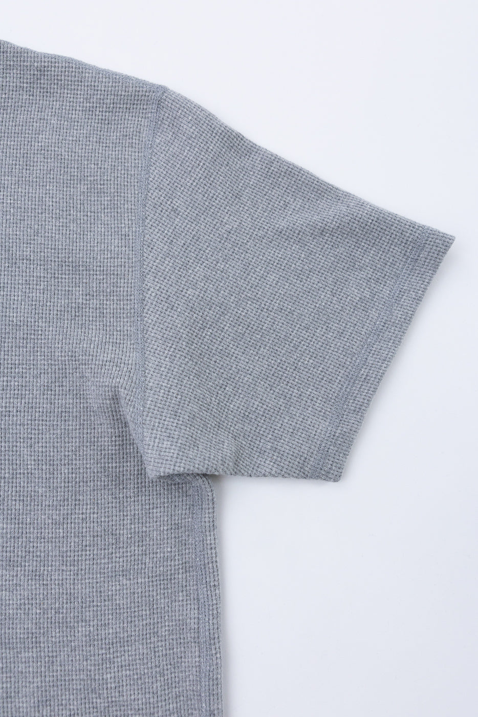 Close-up of the left sleeve and side of a grey waffle knit shirt flat lay.