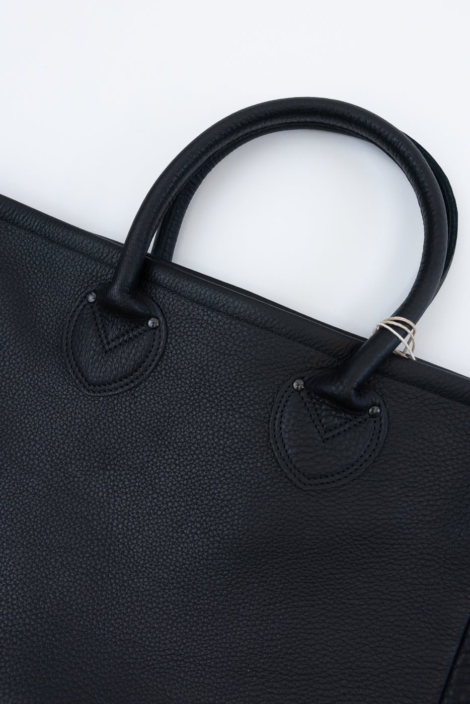 Close-up of black pebbled leather tote bag, front view, showing handles and stitching details