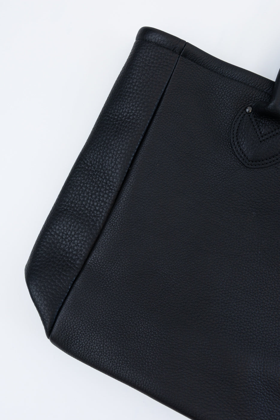 Close-up of black pebbled leather tote bag, front view, showing texture and stitching detail