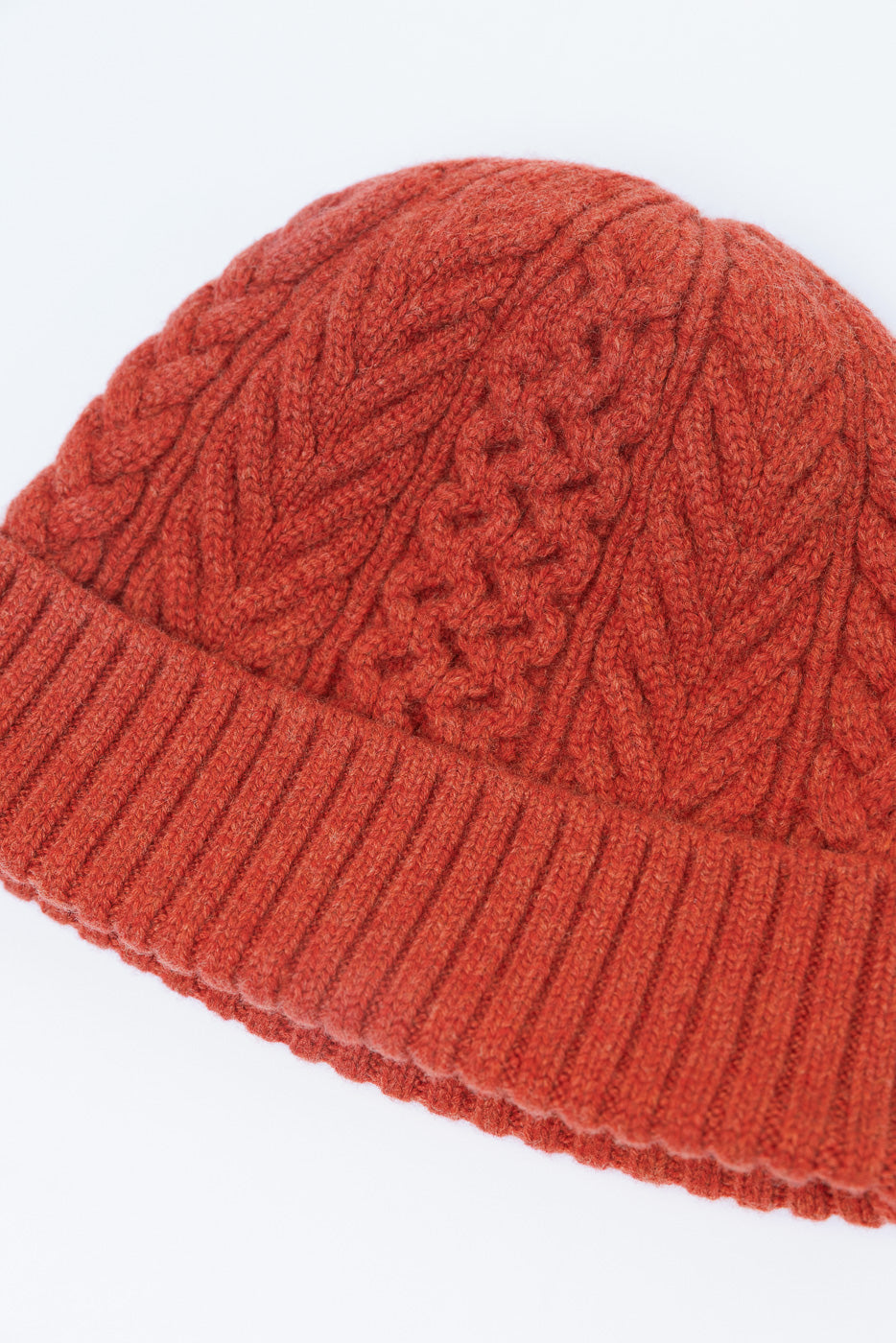 Close-up of the front cable-knit texture and ribbed cuff of a rust-colored beanie.