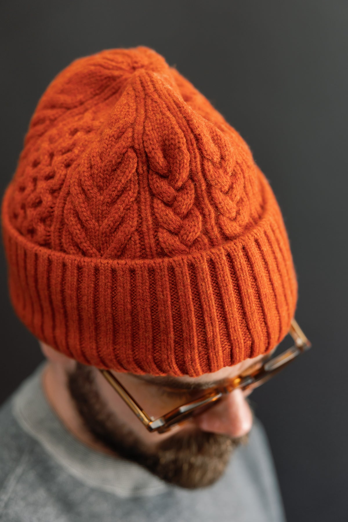 Close-up side view of an orange cable-knit beanie on a male model with a beard.