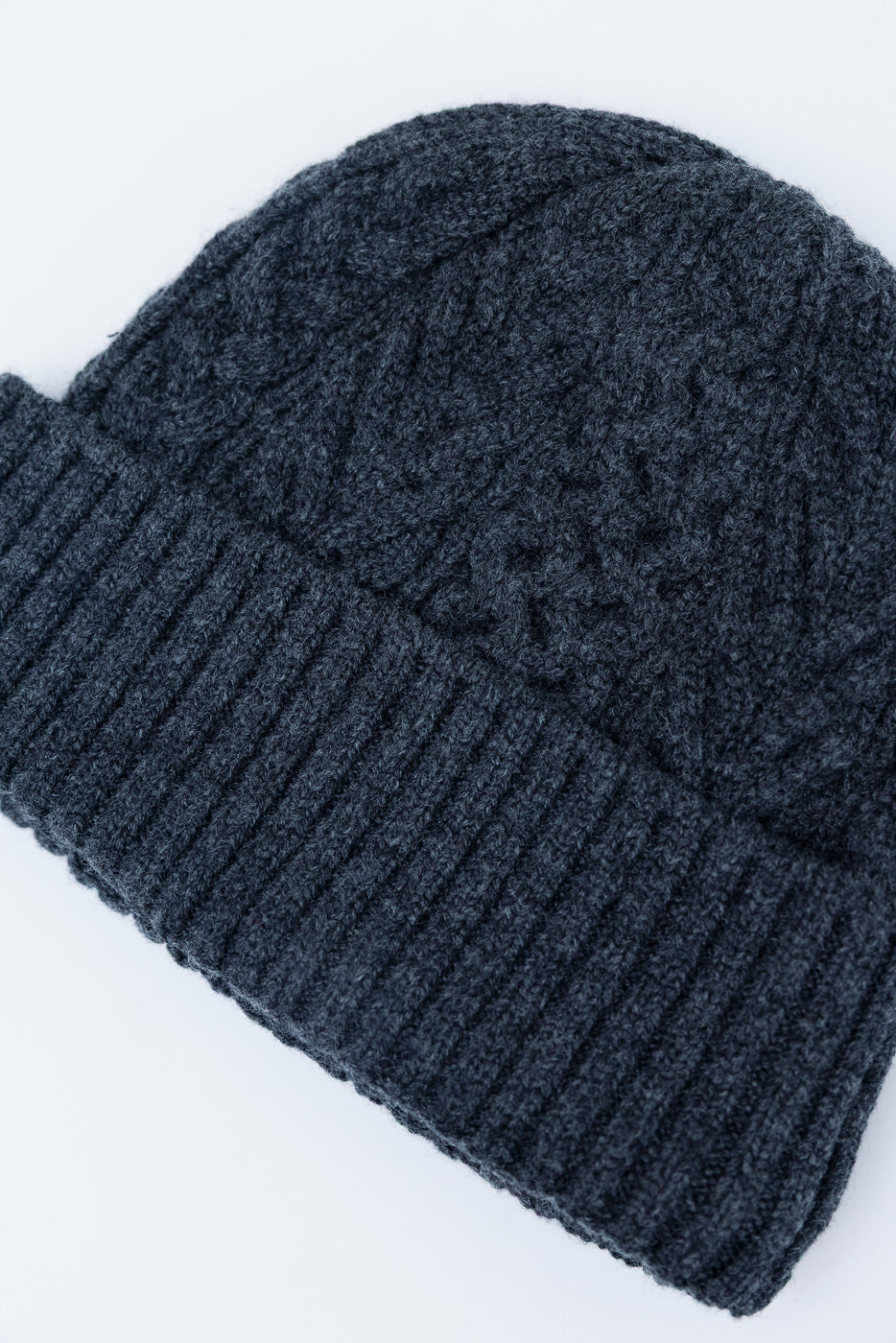 Close-up front view of a dark navy blue cable knit beanie showing thick ribbed cuff and textured pattern.