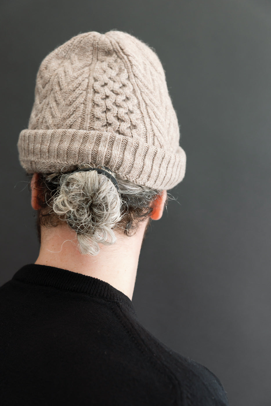 Back view close-up of a tan cable-knit beanie worn by a male model.