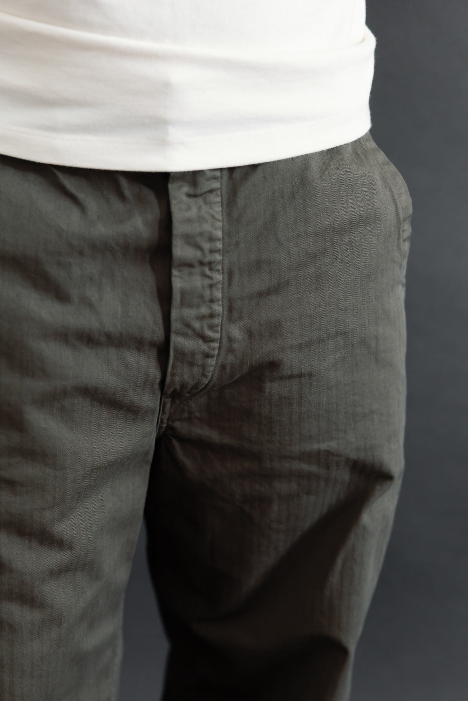 Close-up front view of olive green textured cotton trousers showing the waistband and fly.