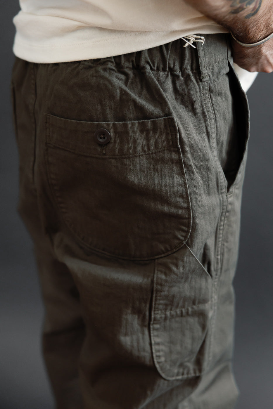 Close-up side view of olive green cargo pants on a male model showing back pocket and side seam.