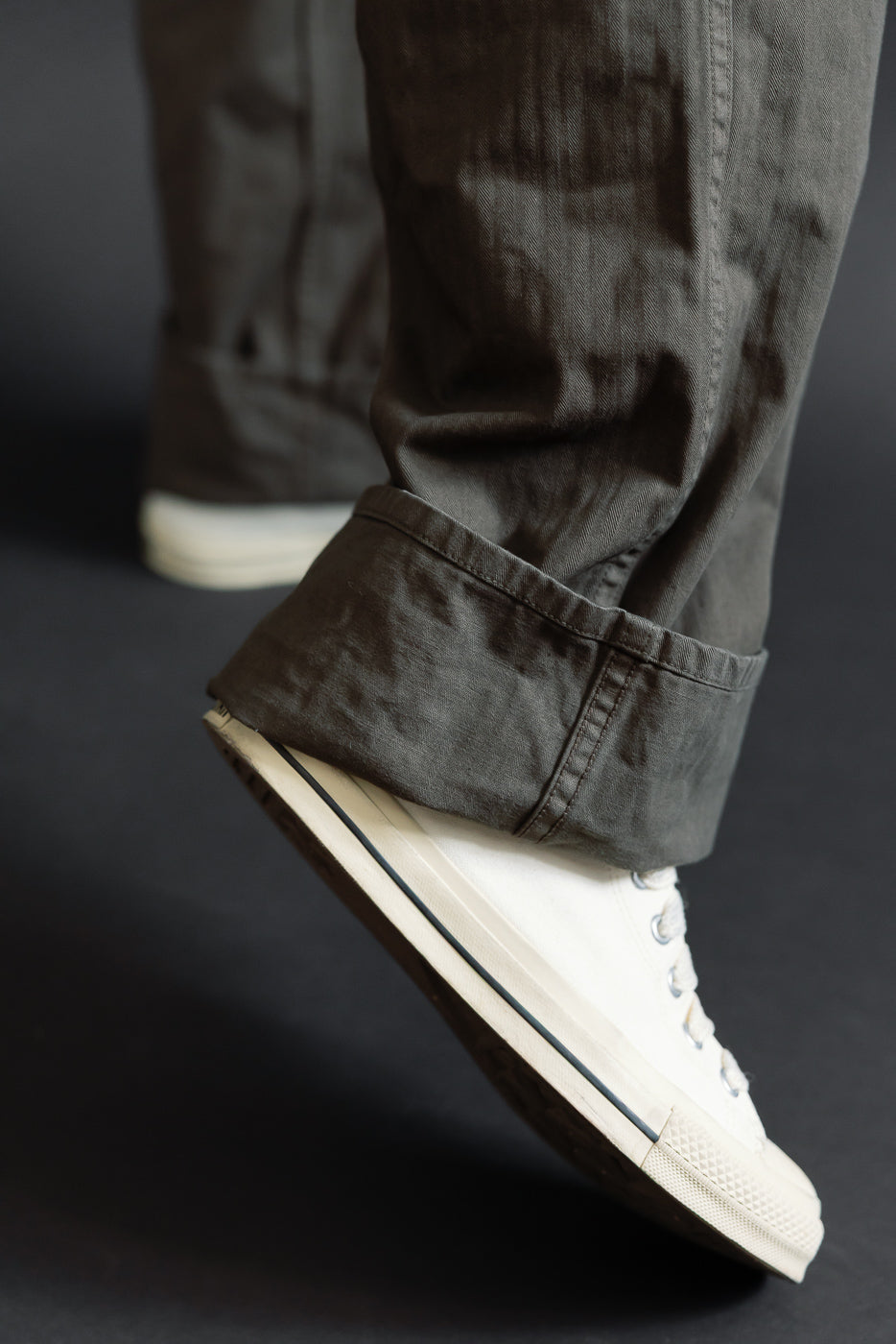 Close-up of the hem and white canvas sneakers worn by a male model.