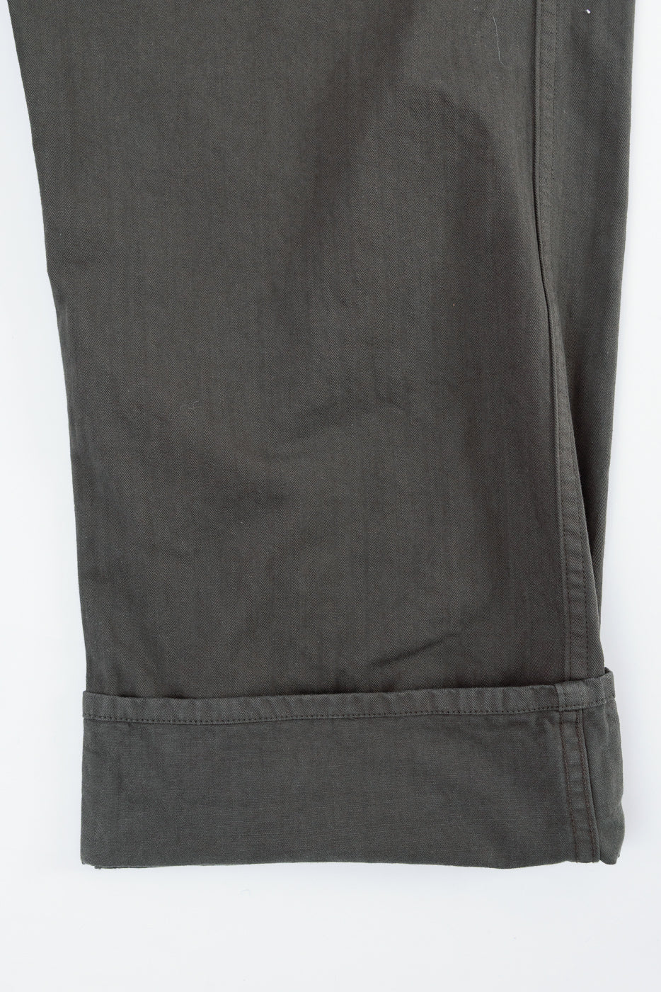 Close-up of the bottom hem and cuffed leg of dark olive green cotton trousers.