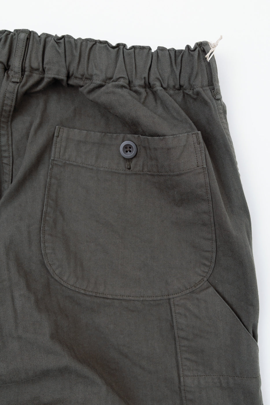 Close-up of the back right pocket of olive green trousers featuring a single button closure.