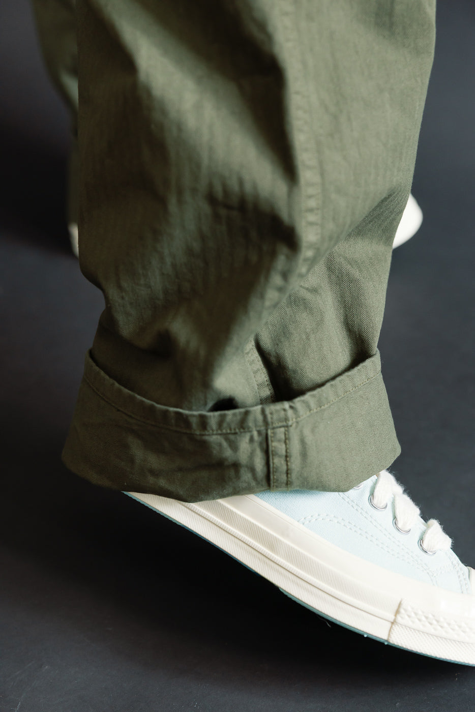 Close-up of male model’s lower leg wearing army green wide French work pant, hem detail visible, side view.