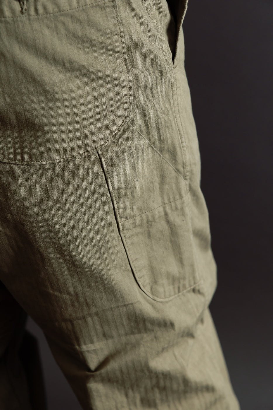 Close-up of the side view and back pocket of khaki canvas utility trousers showing fabric texture.