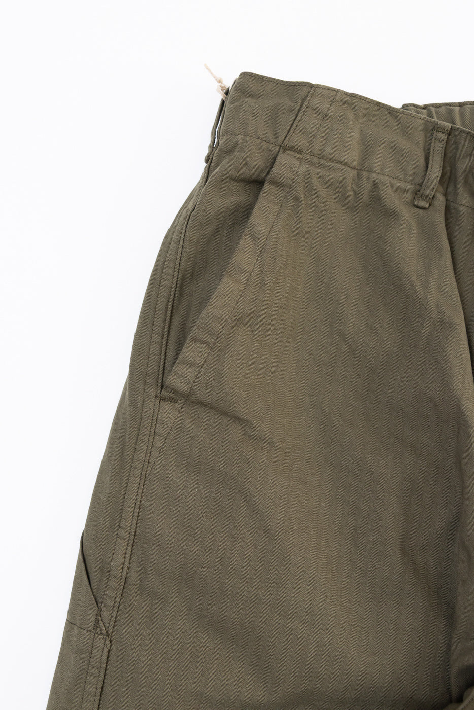 Close-up of the front left side of olive green cotton trousers showing the waistband and pocket.