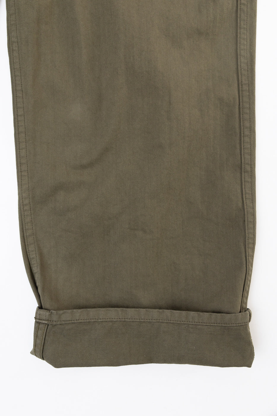 Close-up view of the bottom hem and cuffed leg of olive green cotton trousers, front side.