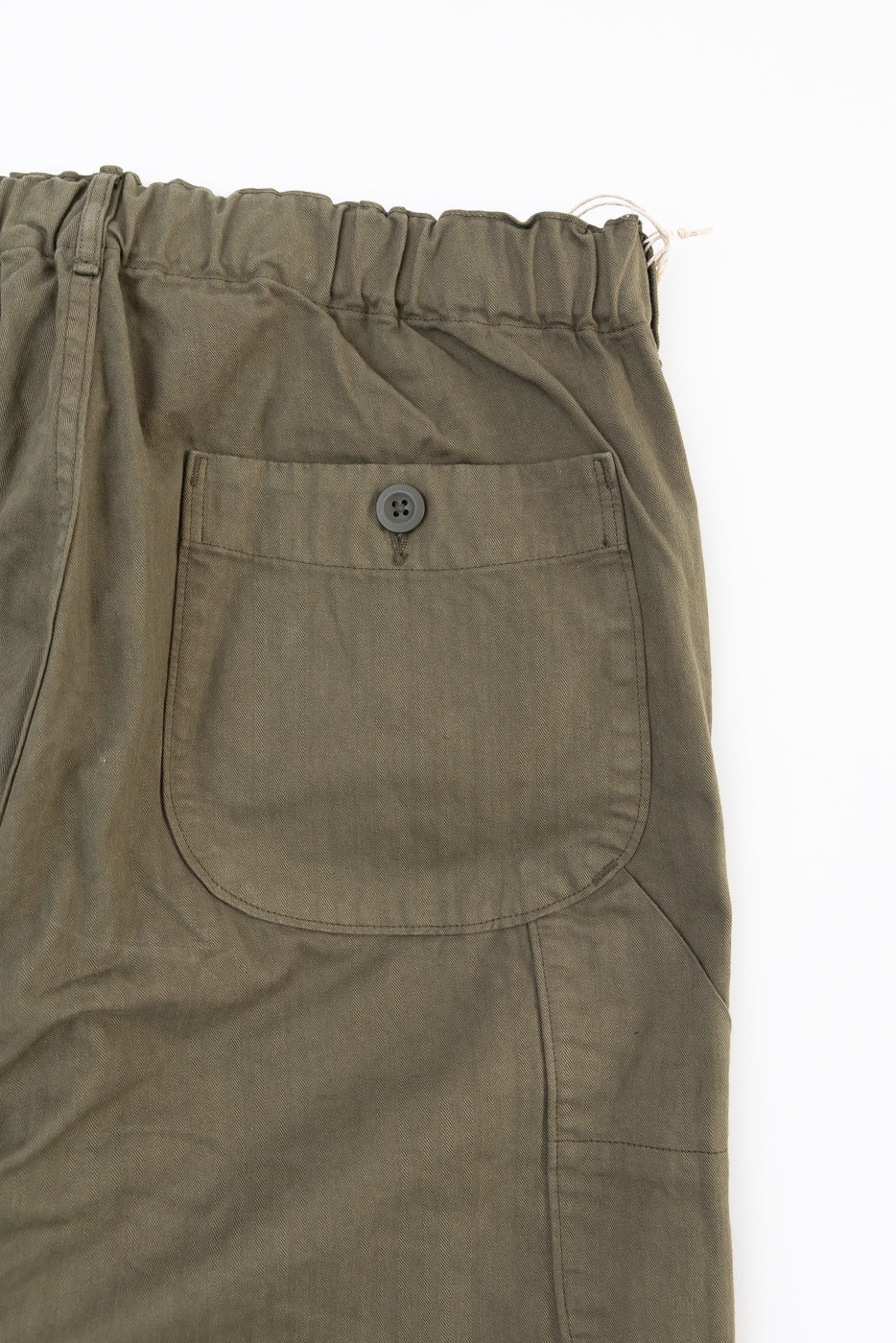 Flat lay close-up of the back right pocket and elastic waistband of olive green cotton trousers.