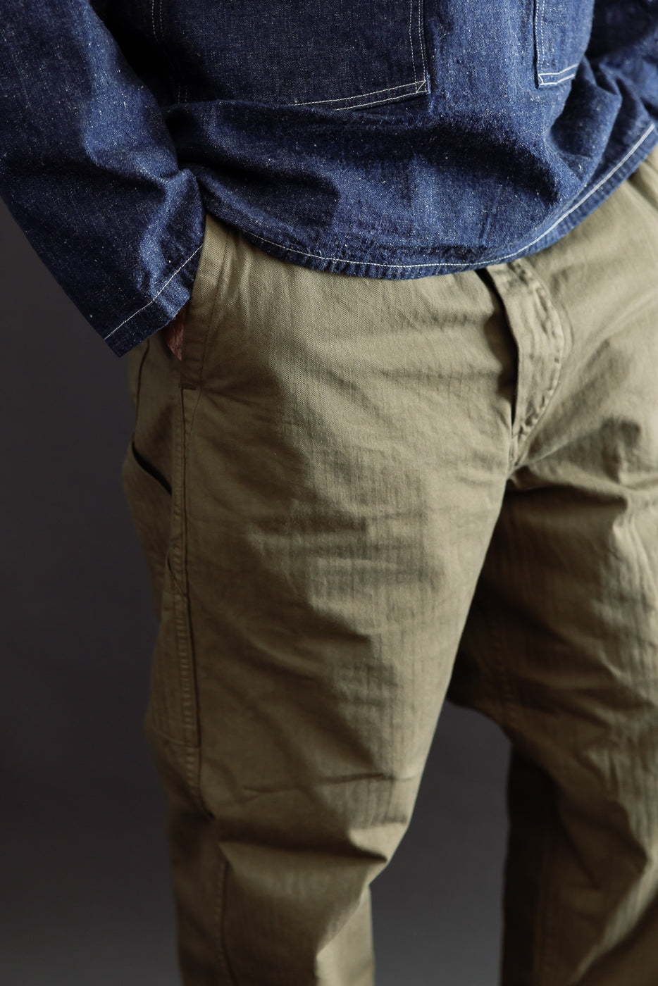 Close-up back view of a male model wearing olive green cargo pants and a dark blue denim shirt.