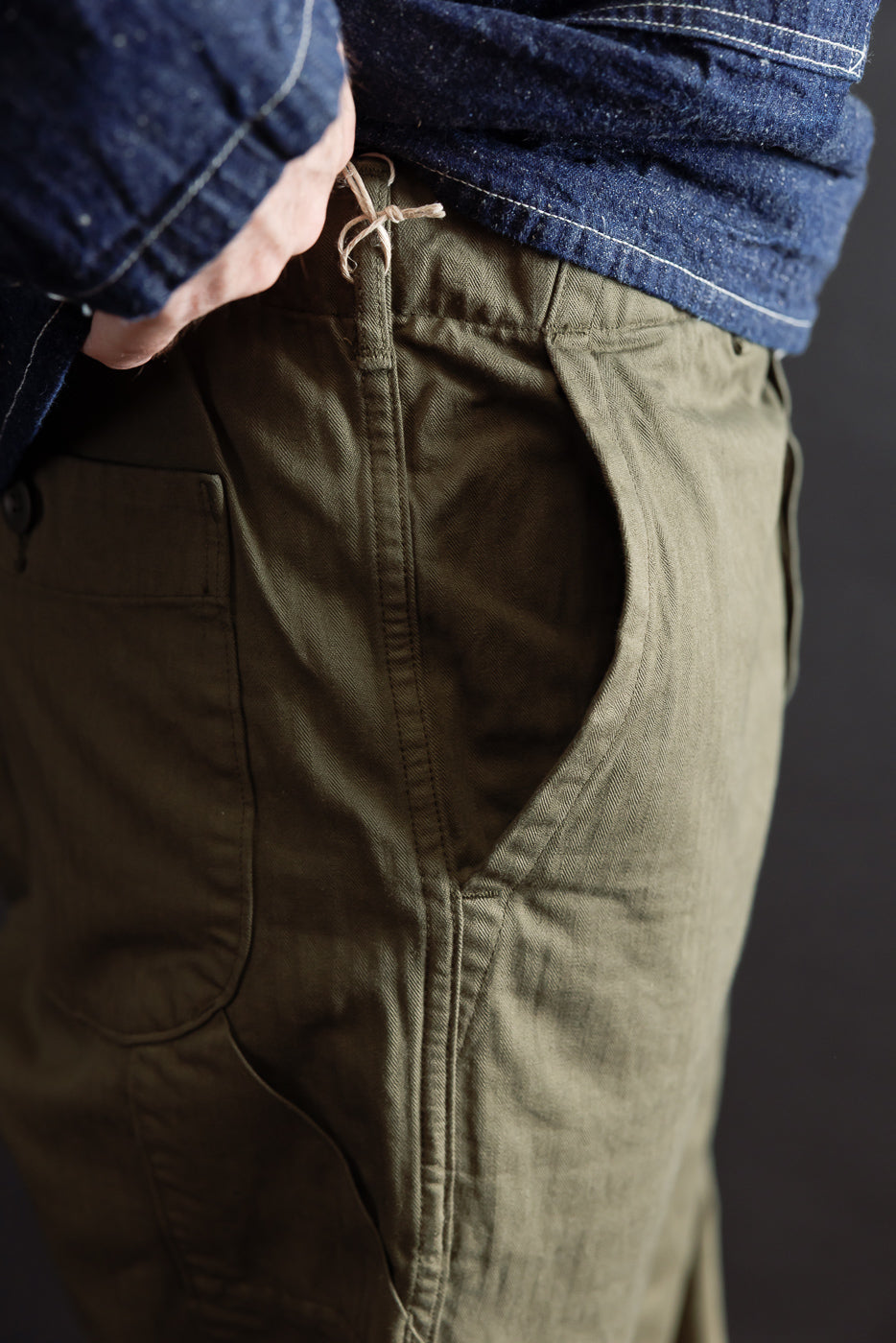Close-up side view of olive green canvas trousers showing pocket detail and drawstring waist.