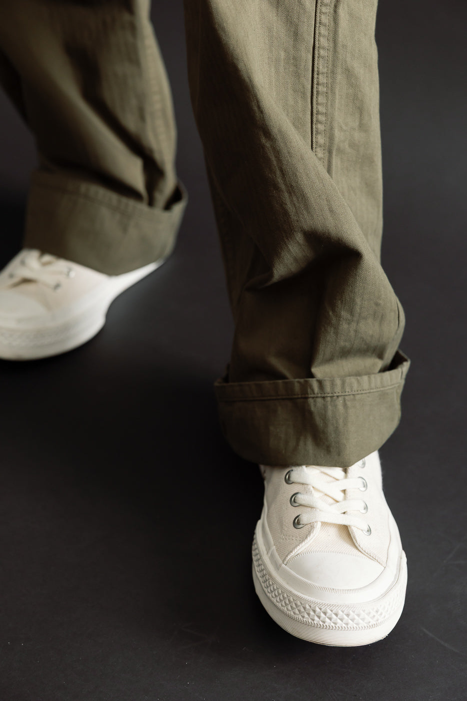 Close-up of a male model's olive green trousers with cuffed hems and white sneakers.